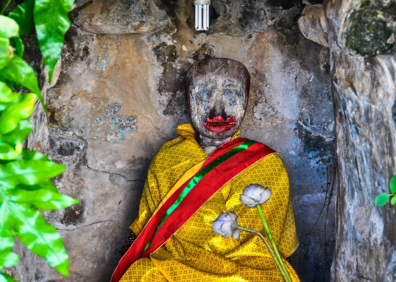 An ancient Cambodian wood statue is wrapped in marigold robes and decorated with lipstick.