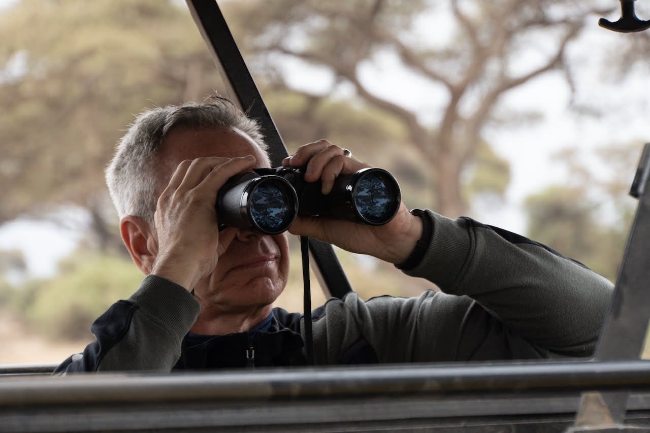 A gay man uses binoculars to spot distant Kenyan wildlife.