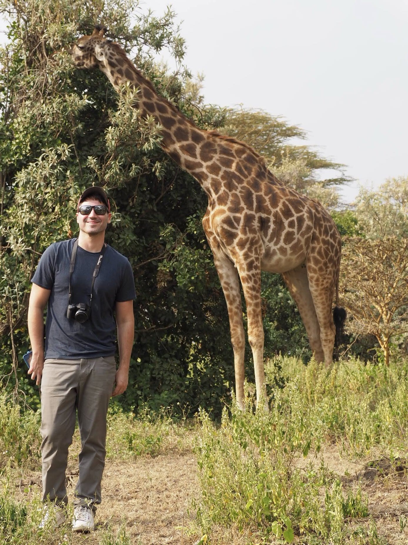 A gay traveller poses in front of a giraffe on Crescent Island.