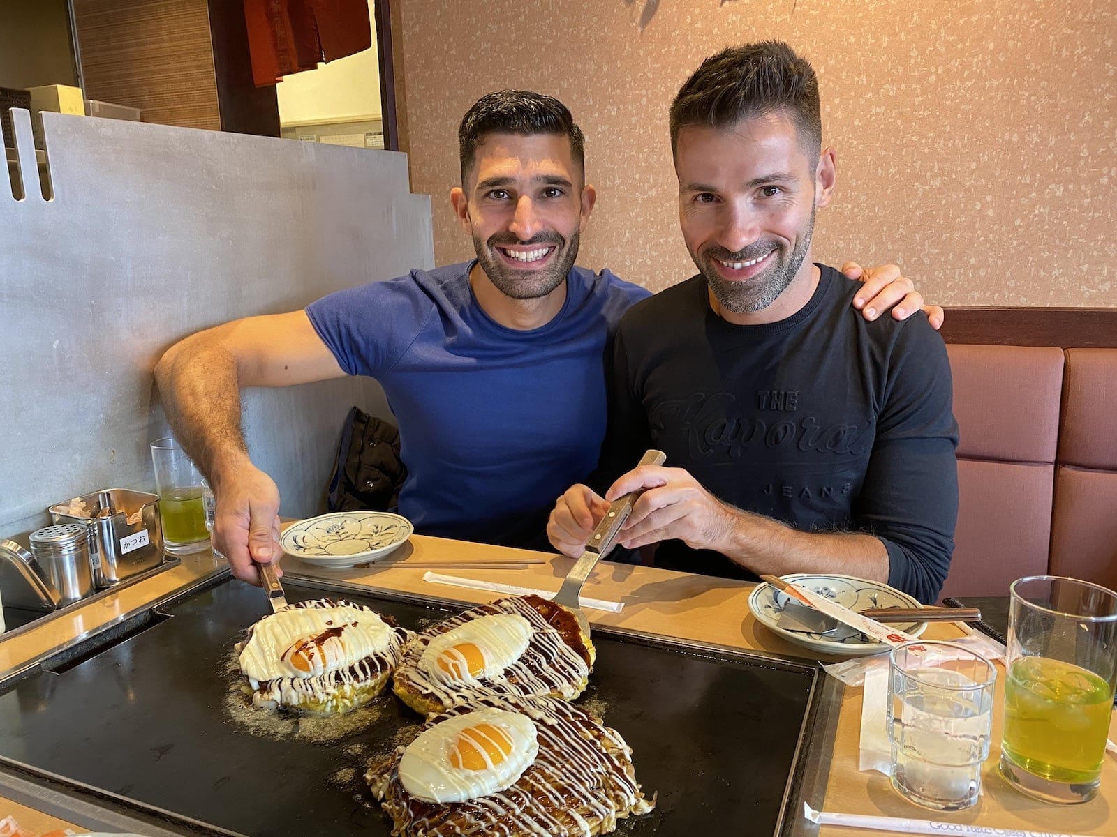 Two gay men enjoying a fried Japanese pancake.