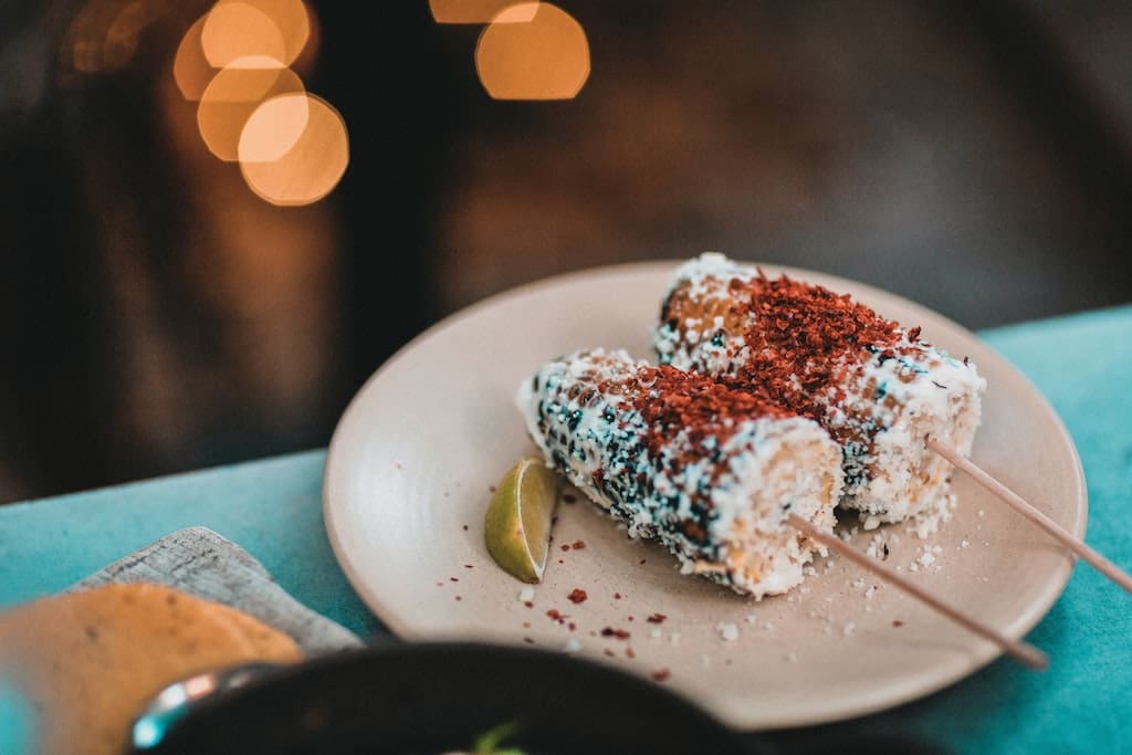 Two skewers of Elotes, or Mexican corn, served with mayo, lime and chili.