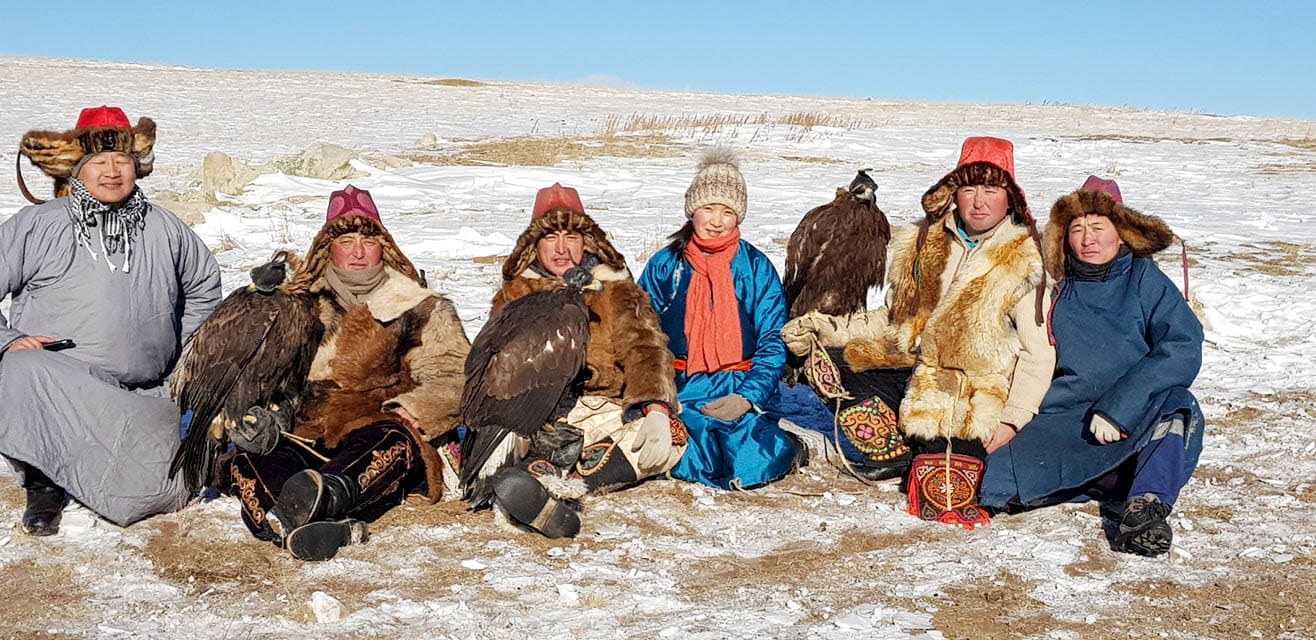 A group of Mongolians sit in the countryside with their pet golden eagles.